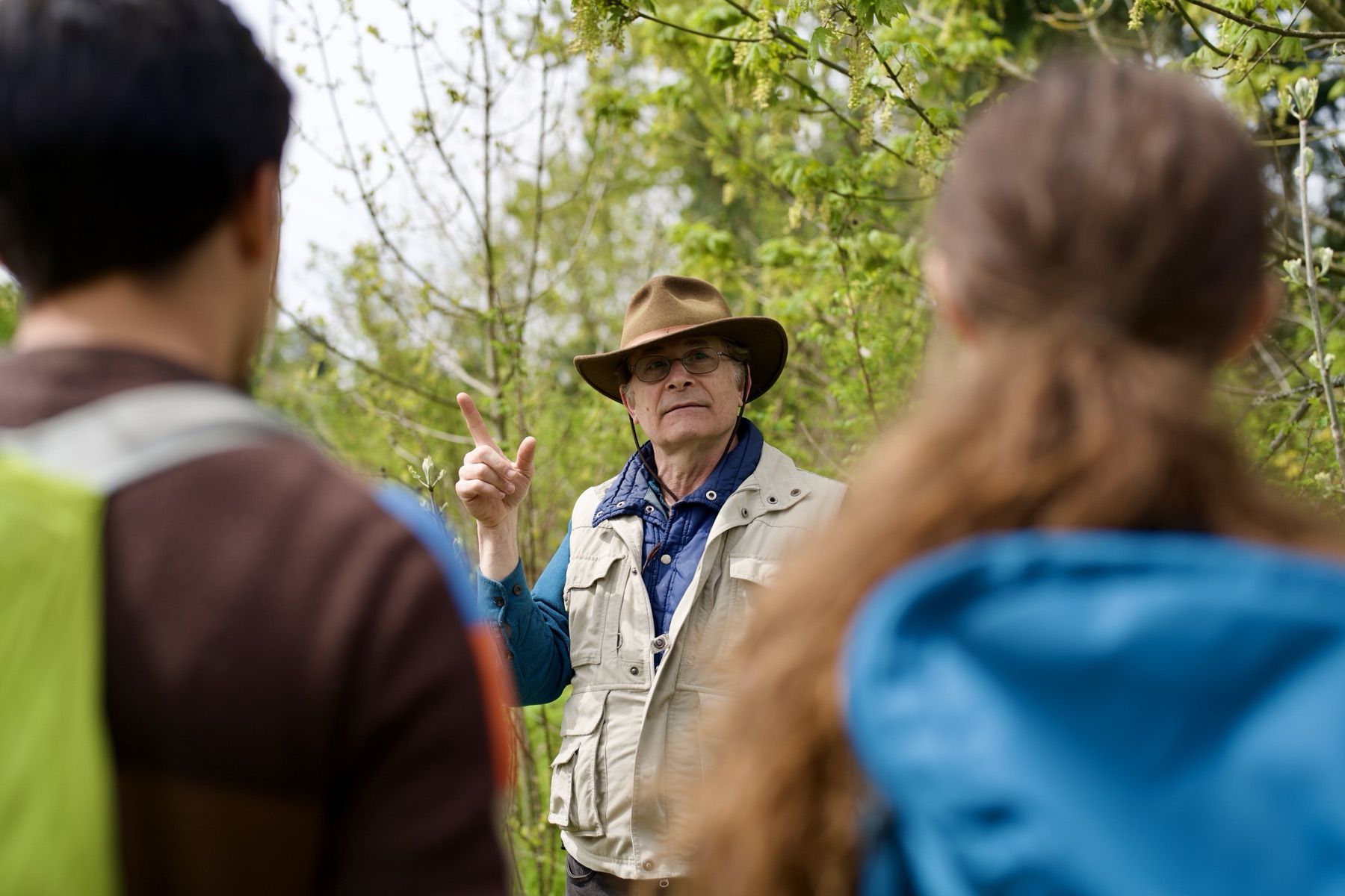 An outdoor educator speaking to two students in a forest.